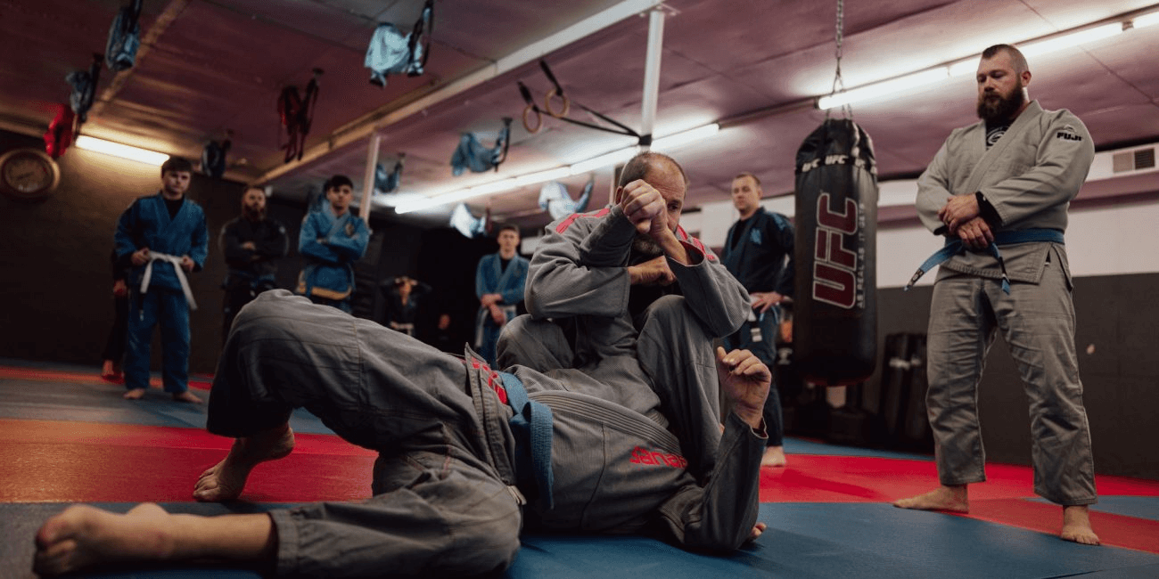 Students watching partner practice on the academy mats